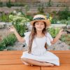 pretty-brunette-female-kid-straw-hat-sitting-near-flowerbed-lotus-pose-with-eyes-closed-little-girl-white-dress-doing-yoga-garden_197531-3985